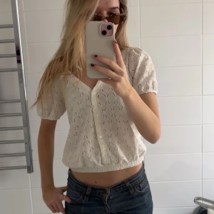 Vit blus från Cache Cache - Säljer en söt vit blus från Cache Cache med korta ärmar och v-ringning. Blusen har ett fint hålmönster och knappar framtill. Perfekt för en somrig look! 🌼