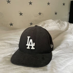 Svart keps från New Era - Snygg svart keps från New Era med vit broderad logga framtill. Klassisk 59FIFTY-modell med platt skärm. Perfekt för en stilren look.