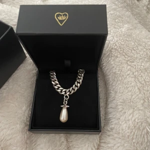 Maria Nilsdotter - Elegant halsband i silverfärg med ett droppformat pärlhänge. Kedjan är kraftig och har en karbinhake för enkel stängning. Perfekt för att ge en stilren touch till din outfit. Helt i nyskick!!!