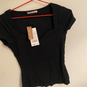 Svart ribbad topp från Anna Field - Snygg svart ribbad topp från Anna Field i ekologisk bomull. Toppen har en v-ringad design och korta ärmar, perfekt för en stilren look. Passar bra till både jeans och kjol.