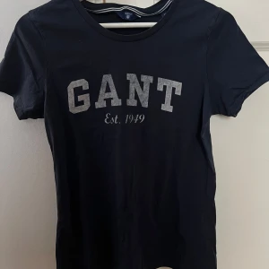 Marinblå t-shirt från GANT - Snygg svart t-shirt från GANT med tryck 'GANT Est. 1949' i grått på framsidan. Perfekt för en casual look. Tillverkad i mjukt material för extra komfort.