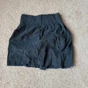 Svart kjol från Zara Basic - Säljer en svart kjol från Zara Basic med en elastisk midja för extra komfort. Kjolen har en avslappnad passform och är perfekt för en stilren look. Den är enkel att matcha med olika toppar och accessoarer.