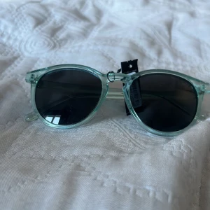 Transparenta solglasögon från Blix för barn - Snygga transparenta solglasögon från Bliz med en modern design. Bågarna är i en ljusgrön nyans och glasen är mörka för att skydda mot solen. Perfekta för en stilren look under soliga dagar. 
