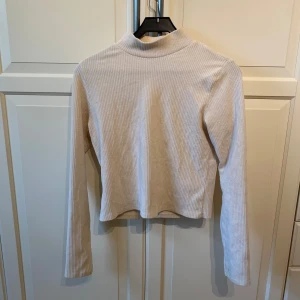 Beige ribbad  polotröja från Gina Tricot - Säljer en beige ribbad polotröja från Gina Tricot i storlek L. Tröjan ät lång ärmad och har en mjuk, stretchig känsla. 