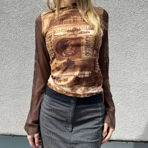 Save The Queen topp - Säljer min Save The Queen brun mesh topp med romerskt inspirerat tryck. Långa transparenta ärmar med blå snörningsdetaljer och stora bokstäver på ena ärmen. Formgivande passform och stretchigt material som kan fungera på storlek XS,S,M. Mycket bra skick!