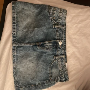Blå jeanskjol från Divided - Säljer en klassisk blå jeanskjol från Divided i kort modell. , bälteshällor och stängs med knapp och dragkedja framtill. Perfekt för dig som gillar en enkel och tidlös stil.storlek 34