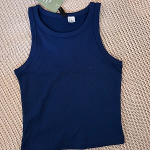 Blå ribbad linnetopp från Divided - Säljer en blå ribbad linnetopp från Divided. Toppen är ärmlös med rund halsringning och har en tight passform. Perfekt för varma dagar eller som lager under andra plagg.