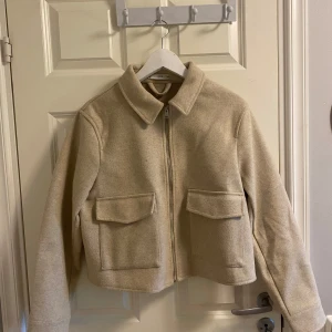 Beige ulljacka från MNG - Säljer en beige jacka från MNG med dragkedja framtill och två stora fickor med lock. Jackan har klassisk krage och är tillverkad i ullblandning. Perfekt för höst och vår, enkel att matcha till olika outfits.