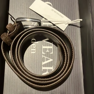 Brunt mockabälte från ONEWear Sweden - Helt oanvänt snyggt brunt bälte i mocka från ONEWear Sweden med silverfärgat spänne. Bältet har en klassisk design med rundad spets och dubbla hällor. Perfekt accessoar för att lyfta din outfit.
