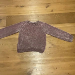 Ljuslila chenilletröja - Mysig ljuslila tröja i chenille med rund halsringning och långa ärmar. Tröjan har ribbade muddar vid ärmslut och nederkant, vilket ger en skön och avslappnad passform. Perfekt för kyligare dagar.