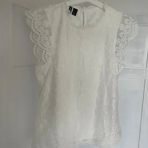 Vit spetsblus  - Säljer en vit blus med vackra spetsdetaljer och volang vid ärmarna. Blusen är ärmlös och har rund halsringning. Perfekt för vår och sommar!Använd endast en gång!💗