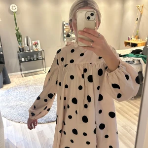 Prickig kortklänning med rosett i ryggen - Säljer en söt kortklänning i ljus beige med stora svarta prickar. Klänningen har lång ärm, lös passform och band i ryggen. Perfekt för dig som gillar lekfulla mönster och oversized stil. Hittar ingen lapp i den men den passar mig som vanligtvis bär xs-s 