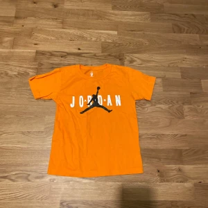 Orange Jordan t-shirt med tryck - Snygg orange t-shirt från Jordan med stort svart logotryck och vit text på bröstet. Klassisk passform och rund halsringning. Perfekt för dig som gillar sportig stil och streetwear.