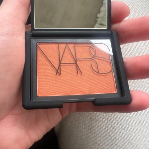 NARS Blush Taj Mahal - NARS blush i nyansen Taj Mahal, en intensiv orange färg med guldig lyster. Kommer i en stilren svart dosa med spegel. Perfekt för att ge kinderna en varm och glowig look.
