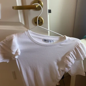 Vit ribbad topp med volangärmar från Zara - Säljer en vit body från Zara, aldrig använd så de inte riktigt va min stil. Verkligen superfin nu till sommaren😄