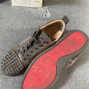 Grå mockasneakers med nitar från Christian Louboutin - Säljer ett par äkta grå sneakers i mocka från Christian Louboutin med svarta nitar på tån och klassisk röd sula. Säljer billigt för de har gått lite sönder i hälen inuti sulan. Perfekt för dig som vill sticka ut med exklusiva detaljer. Några nitar har tappat lite färg, men det kommer med extra nitar så man kan byta