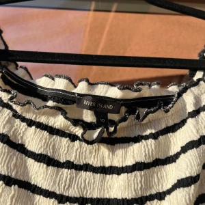 Randig klänning från River Island - Säljer en vit och svart randig klänning från River Island. Klänningen har en tight passform, korta ärmar och smockat material som ger en snygg struktur. Perfekt för dig som gillar en enkel men stilren look.