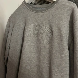 Grå sweatshirt från GANT - Säljer en klassisk grå sweatshirt från GANT med broderad logga framtill. Tröjan har rund halsringning och långa ärmar. Perfekt för en avslappnad och stilren look.