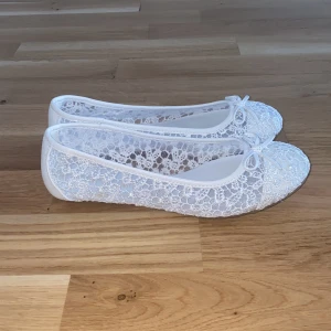 Vita spetsballerinaskor  - Säljer ett par vita ballerinaskor från Graceland med spetsdetaljer och en söt rosett framtill. Skorna har rund tå och platt sula, perfekta till sommarens tillfällen. Lätta och luftiga med elegant spetsmönster. Ej använd endast testade.