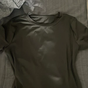 Svart kortärmad topp i skinnimitation - Säljer en svart topp i skinnimitation med rund halsringning och korta ärmar. Toppen  har en enkel och stilren design som ger en cool look. Perfekt för dig som gillar minimalistisk stil.