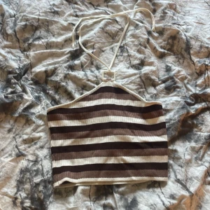 Brun och vit randig topp - Toppen har ribbad struktur och knyts i nacken. Perfekt för varma dagar och enkel att styla med jeans eller kjol.