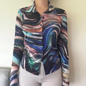 Färgstark mönstrad skjorta - Säljer en skjorta med unikt abstrakt mönster i blått, rosa, grönt och svart. Skjortan har klassisk krage, knäppning framtill och långa ärmar. Perfekt för dig som vill sticka ut med färg och stil.