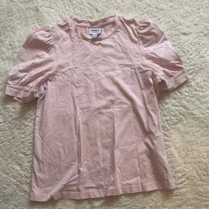 Ljusrosa topp med puffärm från Aware by Vero Moda - Säljer en ljusrosa topp från Aware by Vero Moda. Toppen har korta puffärmar och rund halsringning. Perfekt för dig som gillar en enkel men söt stil.