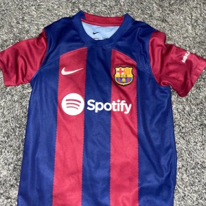 FC Barcelona hemmatröja Nike - Säljer en FC Barcelona hemmatröja från Nike med breda blå och röda ränder, klubbmärke och sponsorlogga på bröstet. Tröjan är kortärmad och har rund hals. Perfekt för dig som älskar Barca! Tröjan är köpt för 1200 i Barcelona shopen i Spanien därför är den 400