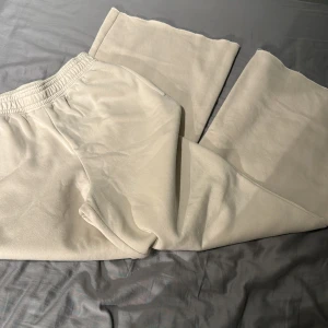 Beige mjukisbyxor från H&M - Säljer ett par beige mjukisbyxor från H&M med resår i midjan. Byxorna har en avslappnad passform och är tillverkade i mjukt material, perfekta för en chill stil. Passar dig som gillar bekväma och enkla plagg.