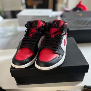 Nike Air Jordan 1 Mid svart/röd/vit - Säljer ett par Nike Air Jordan 1 Mid i svart, eftersom att de inte används längre. Väldigt bra skick, sparsamt använda. Priset är ej hugget i sten, skriv vid minsta fundering eller för mer bilder.