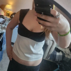 Svart och vit linnetopp - Snygg tvåfärgad linnetopp med breda axelband och markerad byst. Överdelen är svart och nedre delen vit, vilket ger en stilren kontrast. Perfekt att matcha med jeans eller kjol för en trendig look. Inte använd nån gång💕