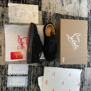 Svarta sneakers från Christian Louboutin - Säljer ett par svarta sneakers från Christian Louboutin med klassisk röd sula. Skorna har snörning, rund tå och är tillverkade i mocka. Perfekta för dig som gillar stilrena och exklusiva skor.