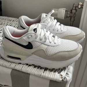 Nike Air Max SYSTM - Snygga vita sparsamt använda Nike Air Max sneakers med mesh- och mockadetaljer. Skorna har svart swoosh, tjock vit sula och röda innersulor. 