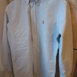 Blårandig skjorta från Ralph Lauren - Klassisk blårandig skjorta från Ralph Lauren med broderad logga på bröstet. Skjortan har lång ärm, knappar framtill och krage. Perfekt för en stilren look och passar till många tillfällen.