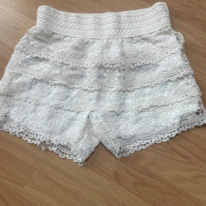 Vita virkade shorts från FB Sister - Stretchiga Superfina vita virkade shorts från FB Sister med blommigt spetsmönster och elastisk midja. Perfekta för sommaren med sin feminina look och snygga detaljer längs kanterna.