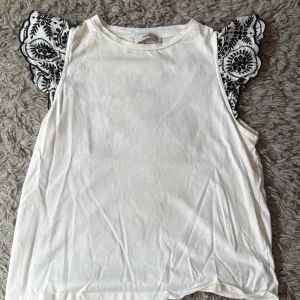 Vit topp med broderade volangärmar - Vit tröja med svart mönster vid axlarna 