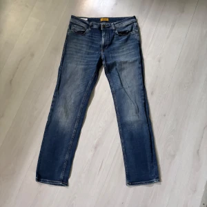 Jack and Jones jeans  - Klassiska blå jeansbyxor från Jack and Jones  med raka ben och femficksmodell. Jeansen har en lätt tvättad look och normal passform. Perfekta för en avslappnad stil och passar till det mesta i garderoben.