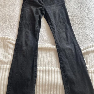 Svarta bootcut jeans med fickdetaljer - Snygga svarta jeans med bootcut passform och coola bakfickor med lock och knapp. Jeansen har en klassisk femficksdesign och är tillverkade i stretchigt denim för en bekväm känsla. Perfekta till sneakers eller boots. Man kan också justera midjan. Jeansen är egentligen i storlek 158 men skulle nog klassas som xxs