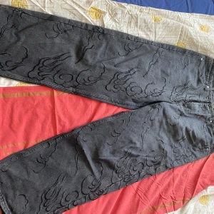 Ed Hardy x Urban Outfitters jeans - Jeans från Ed Hardy x Urban Outfitters med brodering över hela byxorna och gul brodyr på bakfickan. Jeansen har rak och baggy passform.