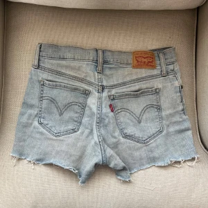 Levi's ljusblå jeansshorts med fransar - Ljusblå jeansshorts från Levi's med råa, fransiga kanter och klassiska bakfickor med logga. Modellen är low/midwaist och har en avslappnad passform. Perfekta för sommaren och enkla att styla till allt. Snygg slitning och klassisk denimlook.🩵