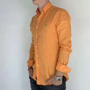Ralph Lauren Linne Skjorta - Nu har vi nöjet att erbjuda en klassisk linne skjorta från det välkända varumärket Ralph Lauren. Plagget är i storlek Small och är i mycket gott skick, utan några synliga defekter. Modellen på bilden är 180 cm lång och väger 75 kg, vilket kan ge en god indikation på tröjans passform.
