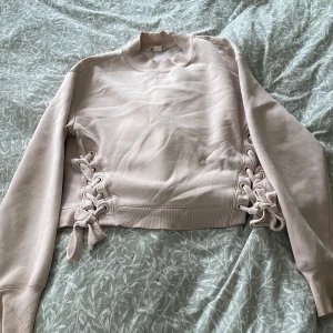 Rosa  sweatshirt med snörning H&M - Superfin rosa sweatshirt från H&M med snygg snörning i sidorna. Tröjan har långa ärmar, ribbade muddar och en relaxed fit. Perfekt för dig som gillar unika detaljer. Liten minimal fläck finns också, men inget man ser tydligt. 