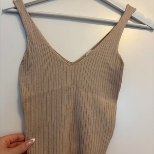 Beige ribbad linnetopp från H&M - Säljer en beige ribbad linnetopp från H&M. Toppen har smala axelband, v-ringning och är figurnära i modellen. Perfekt att styla med jeans eller kjol för en clean look. Materialet är mjukt och stretchigt för extra komfort.
