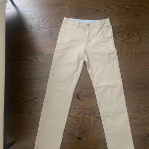 Beige byxor från Polo Ralph Lauren - Snygga beige byxor från Polo Ralph Lauren i klassisk rak modell. Byxorna har diskreta bakfickor med knapp och är tillverkade i mjuk bomull. Perfekta för en clean och stilren look. Pris kan diskuteras 