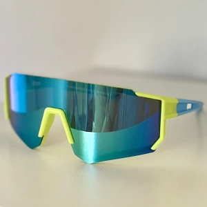 Blå sportiga barn solglasögon - Säljer ett par futuristiska solglasögon med spegelblått, stort visirformat glas och neon-gula detaljer runt bågar och näsbrygga. Skalmarna är blå och har en sportig design. Perfekta för dig som vill sticka ut och gillar en modern vibe🤵🏼