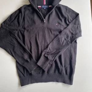 Svart half zip tröja Tommy Hilfiger - Svart långärmad tröja från Tommy Hilfiger med half zip och liten broderad logga på bröstet. Klassisk ribbad mudd vid ärmslut och nederkant. Perfekt för en stilren och avslappnad look. Säljer för 200kr