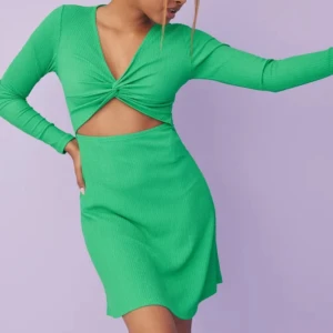Grön cut out klänning från ONLY XS - Snygg grön kortklänning från ONLY i ribbat material. Klänningen har lång ärm, v-ringning och twistad detalj framtill med cut out över magen. Perfekt för dig som vill sticka ut med en trendig look.