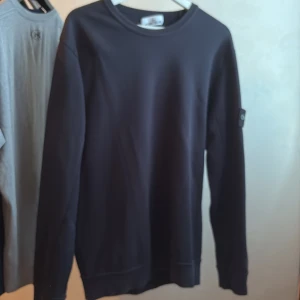 Mörkblå Stone Island sweatshirt - Säljer en svart sweatshirt från Stone Island med klassisk rund hals och lång ärm. Tröjan har den ikoniska loggan på vänster ärm och är tillverkad i mjuk bomull. Perfekt för dig som gillar stilrena och snygga plagg med streetkänsla. M eller L den är ganska stor