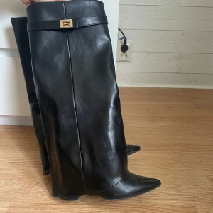 Svarta höga stövlar med spetsig tå - Snygga svarta stövlar i skinn med spetsig tå och låg klack. De har en stilren design med ett dekorativt spänne upptill.  Fick i julklapp så vet inte vart dom är ifrån. Använt endast 1 gång så super bra skick!