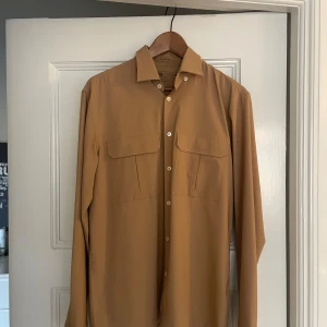 Beige skjorta från Zara Traveler M - Snygg beige skjorta från Zara Traveler-kollektionen i regular fit. Skjortan har två stora bröstfickor med lock, klassisk krage och knäppning framtill. Tillverkad i ett stretchigt och andningsbart syntetmaterial som är skrynkelfritt och luktfritt.